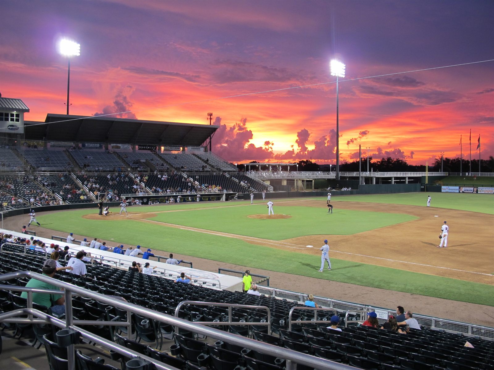 A minor league baseball game under the lights at a stadium as the sky turns red at sunset